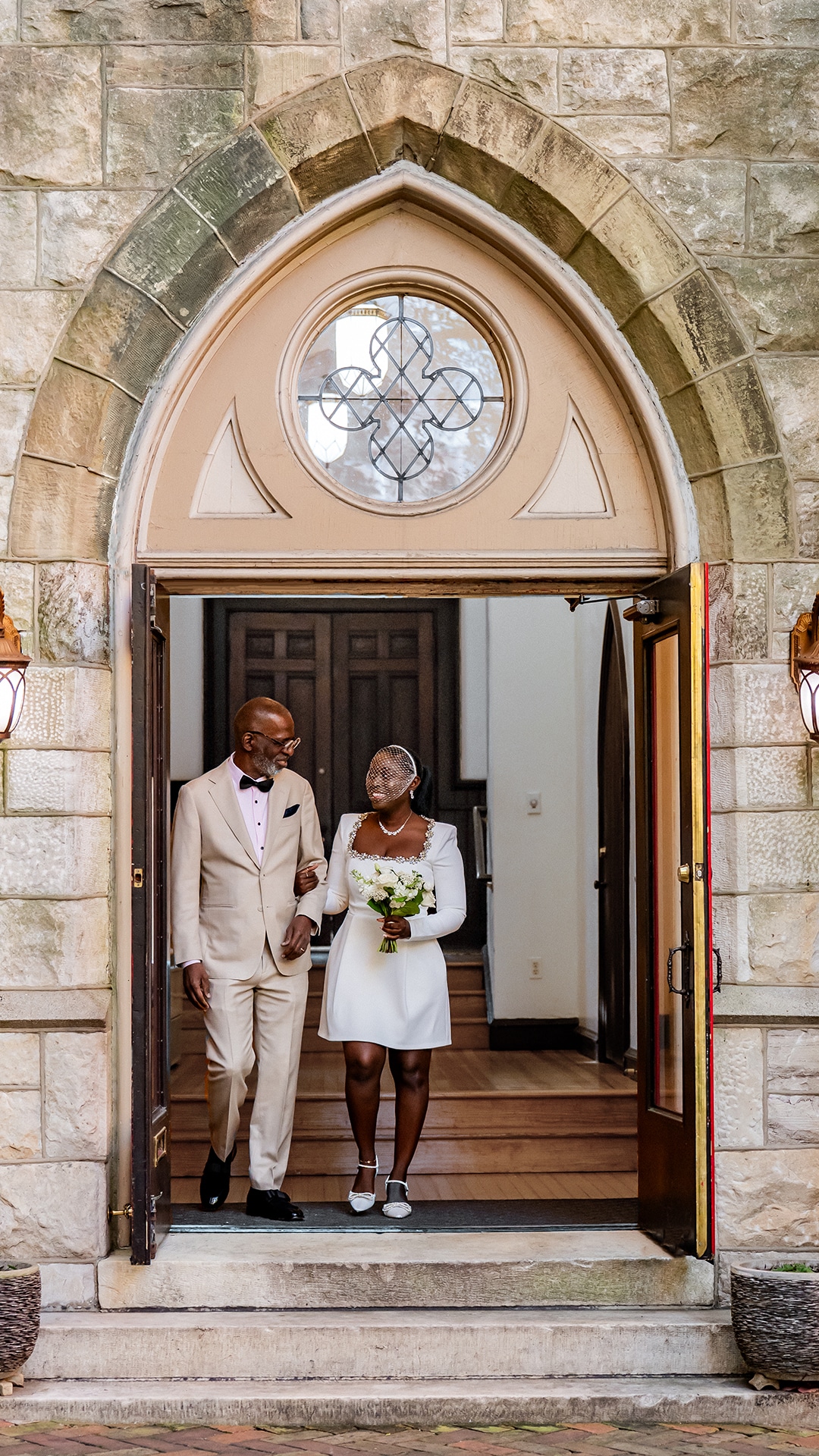 Black bride and her father walking in the gothic doorway at Chase Court in Baltimore, Maryland.
